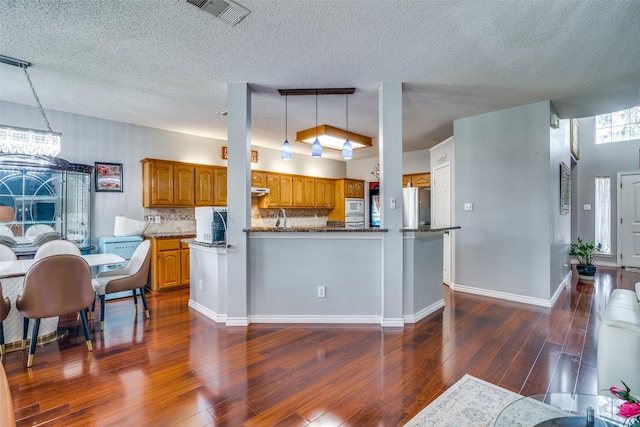 kitchen with decorative light fixtures, visible vents, brown cabinetry, built in microwave, and a peninsula