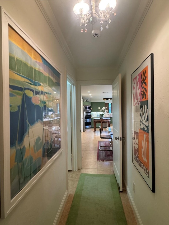 hallway with ornamental molding, a notable chandelier, baseboards, and light tile patterned floors