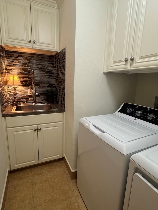 clothes washing area featuring cabinet space, baseboards, washer and clothes dryer, wet bar, and a sink