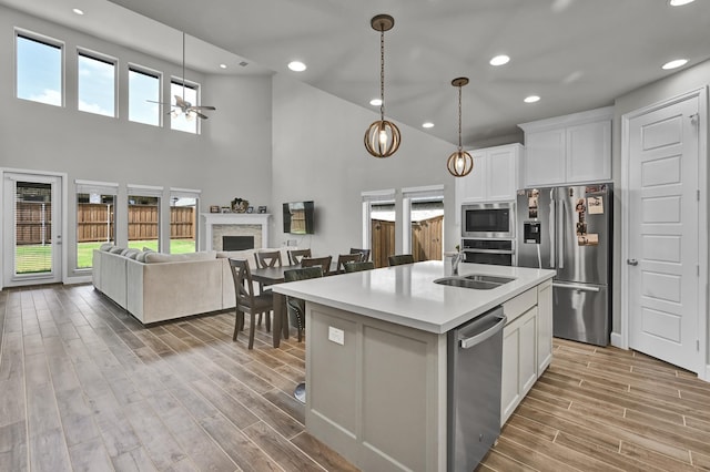 kitchen featuring stainless steel appliances, a sink, white cabinetry, open floor plan, and a center island with sink