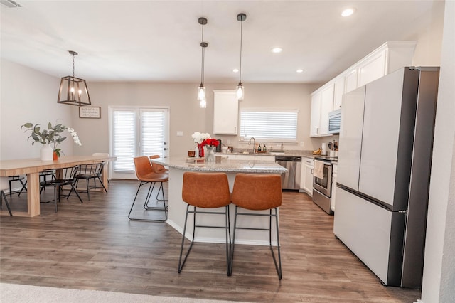 kitchen featuring a center island, pendant lighting, appliances with stainless steel finishes, white cabinetry, and light stone countertops