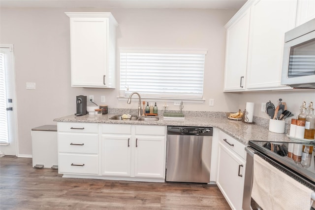 kitchen with appliances with stainless steel finishes, white cabinetry, a sink, and light stone countertops