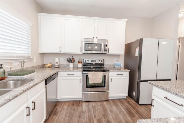 kitchen featuring light stone counters, a sink, white cabinets, appliances with stainless steel finishes, and light wood finished floors