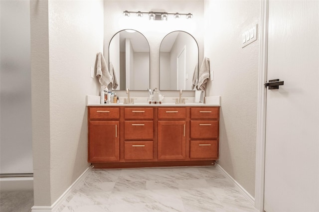 full bathroom with marble finish floor, double vanity, a sink, and baseboards