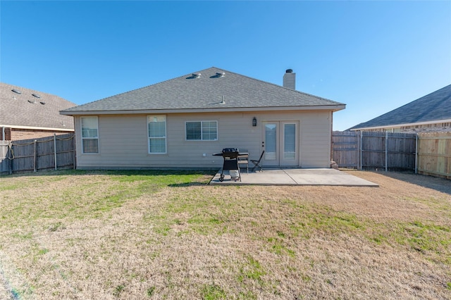 rear view of house with a fenced backyard, a shingled roof, a yard, a chimney, and a patio area