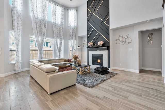 living room with light wood finished floors, a high ceiling, baseboards, and a fireplace