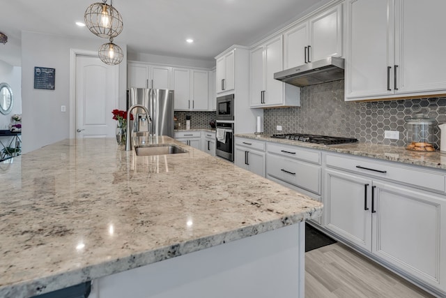 kitchen featuring decorative light fixtures, appliances with stainless steel finishes, white cabinets, a sink, and under cabinet range hood