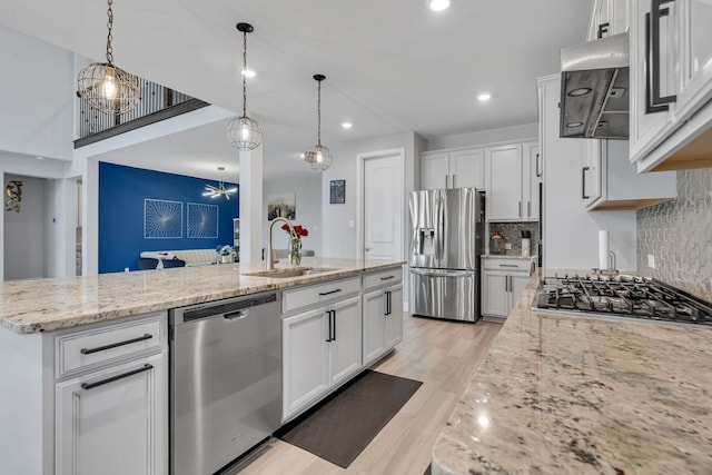 kitchen featuring a center island with sink, stainless steel appliances, white cabinetry, a sink, and light stone countertops