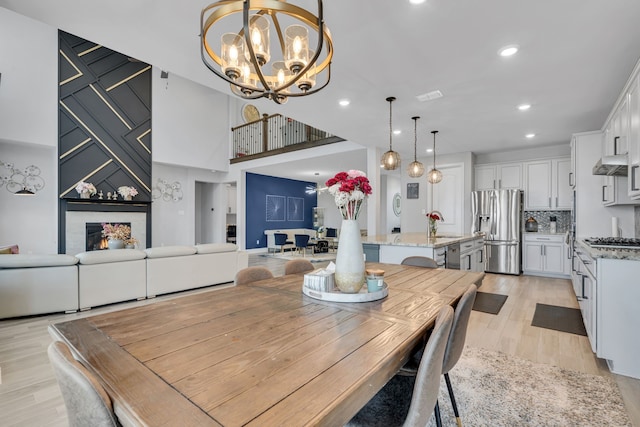 dining space with recessed lighting, a large fireplace, visible vents, light wood-style floors, and an inviting chandelier