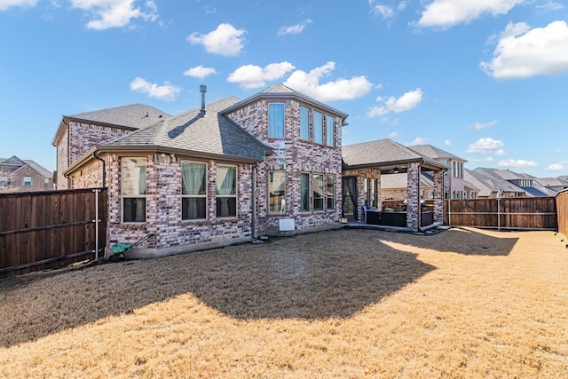 back of property with a shingled roof, a patio area, a fenced backyard, and a lawn