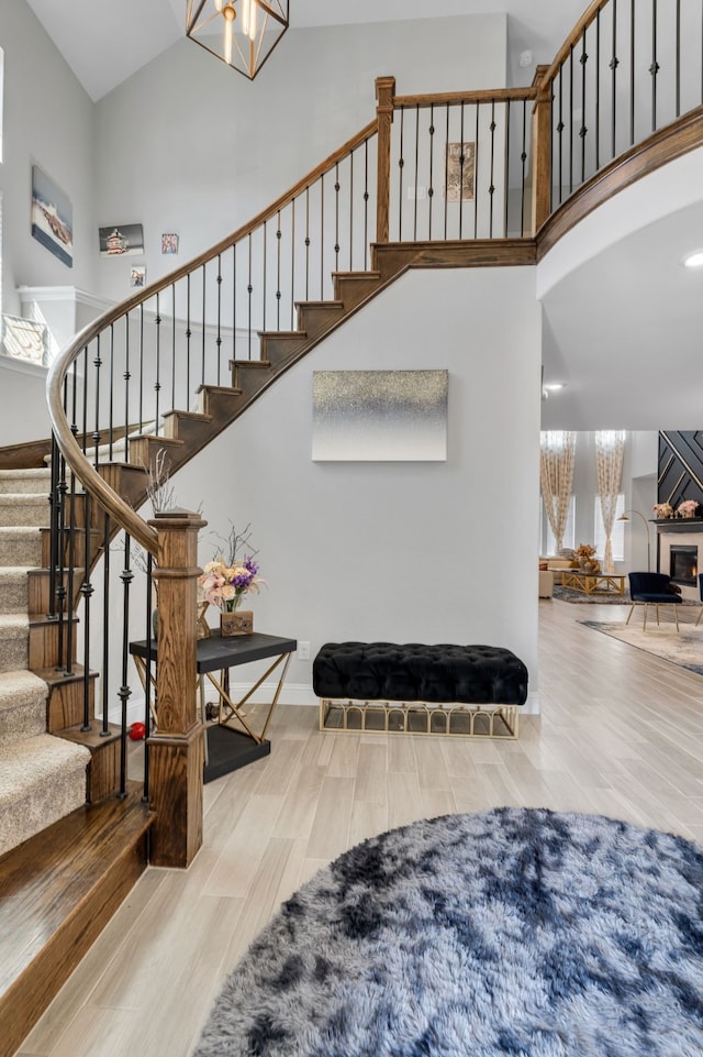 stairs featuring a lit fireplace, a high ceiling, and wood finished floors