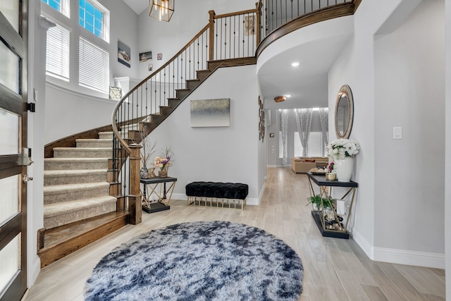 foyer entrance featuring light wood-style floors, stairs, a high ceiling, and baseboards