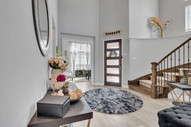 foyer entrance featuring baseboards, a towering ceiling, light wood finished floors, and stairs