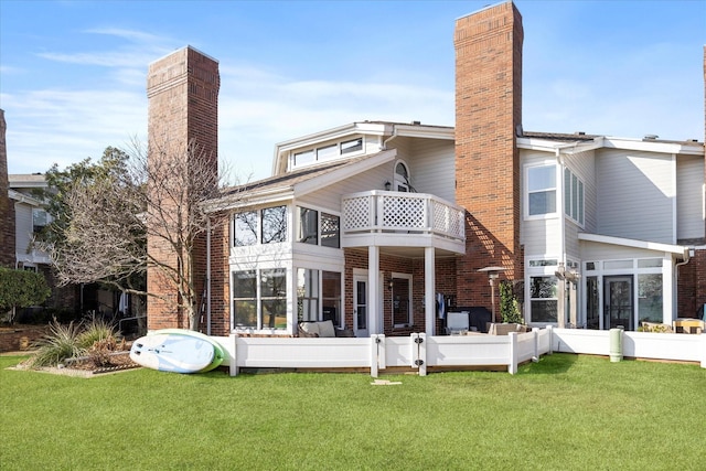 rear view of property featuring brick siding, a yard, a chimney, and a balcony