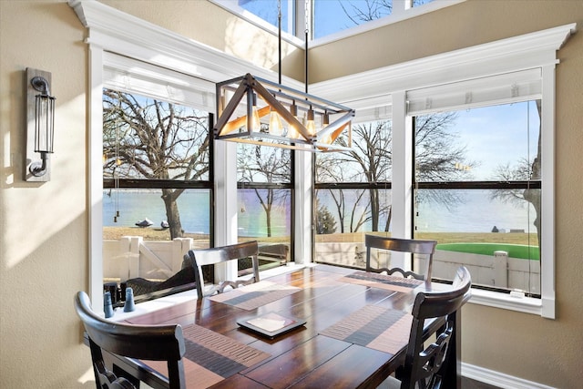 dining area with a chandelier, a water view, a textured wall, and baseboards