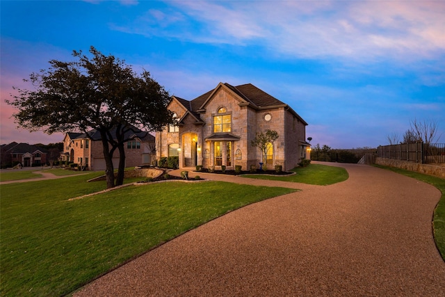 french country style house with stone siding, driveway, fence, and a lawn