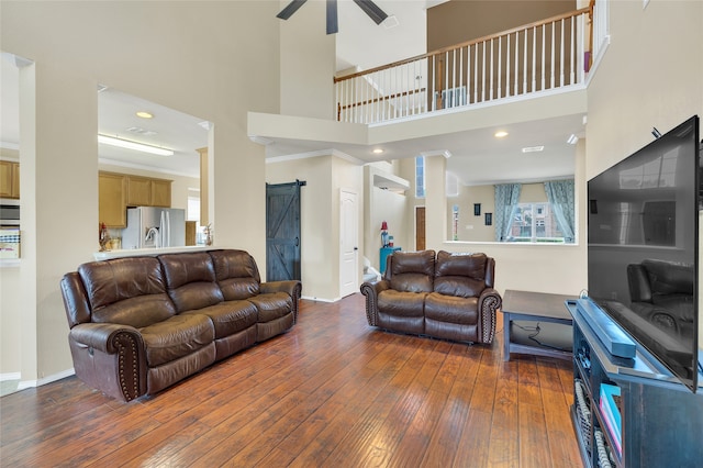 living room with a barn door, visible vents, baseboards, a ceiling fan, and hardwood / wood-style flooring