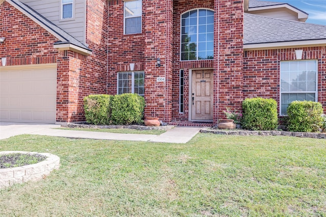 entrance to property with an attached garage, brick siding, a lawn, and roof with shingles