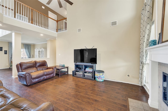 living room with a tile fireplace, wood-type flooring, visible vents, and a towering ceiling