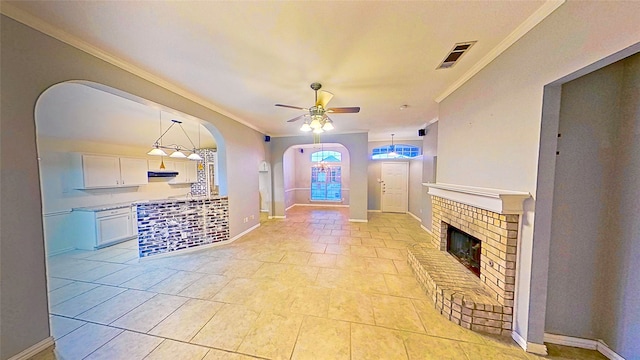 entryway featuring arched walkways, visible vents, ornamental molding, a brick fireplace, and ceiling fan