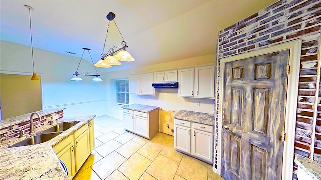 kitchen with light tile patterned floors, a sink, white cabinets, light stone countertops, and decorative light fixtures