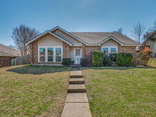 ranch-style home featuring brick siding, roof with shingles, a front yard, and fence