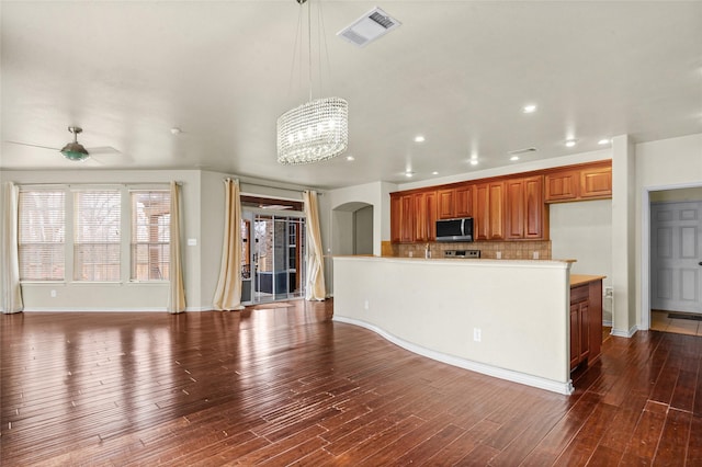 kitchen featuring visible vents, light countertops, hanging light fixtures, stainless steel microwave, and an island with sink