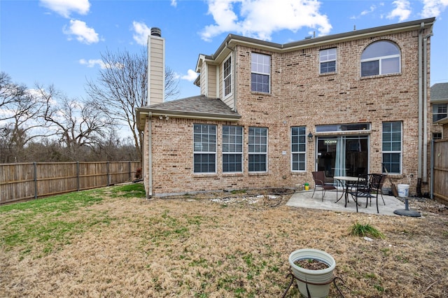 rear view of property with a fenced backyard, brick siding, a yard, a chimney, and a patio area