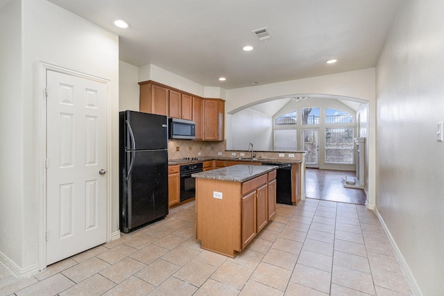 kitchen with visible vents, a center island, stone counters, black appliances, and a sink