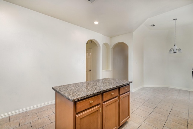 kitchen featuring light tile patterned floors, a kitchen island, dark stone counters, brown cabinetry, and pendant lighting