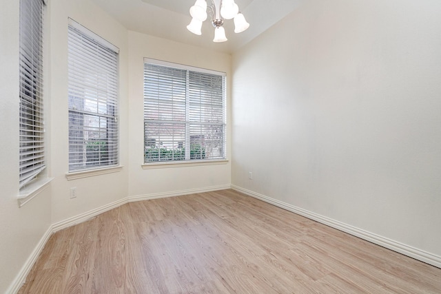 empty room with light wood-type flooring, a notable chandelier, and baseboards