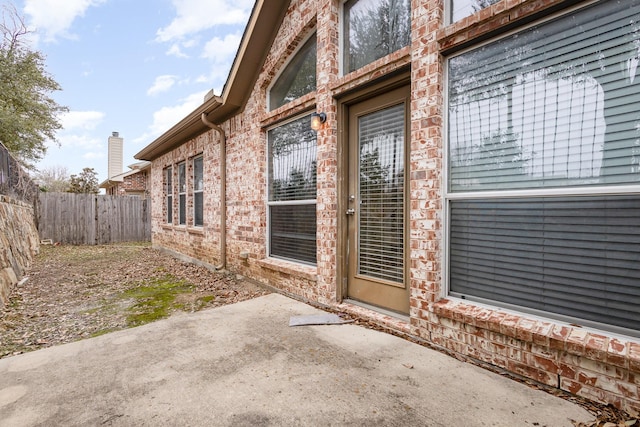 entrance to property with brick siding, a patio area, and fence