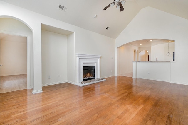 unfurnished living room featuring a warm lit fireplace, light wood finished floors, ceiling fan, and visible vents