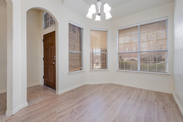 interior space featuring arched walkways, baseboards, light wood finished floors, and an inviting chandelier