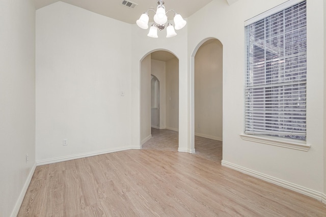 empty room with a chandelier, light wood-type flooring, arched walkways, and baseboards