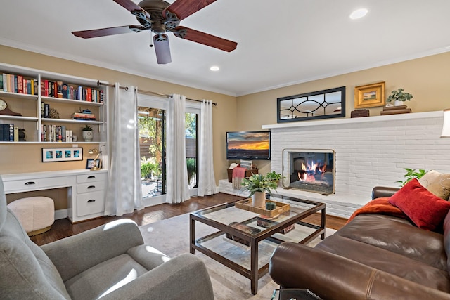 living room featuring ornamental molding, built in desk, a brick fireplace, and dark wood finished floors