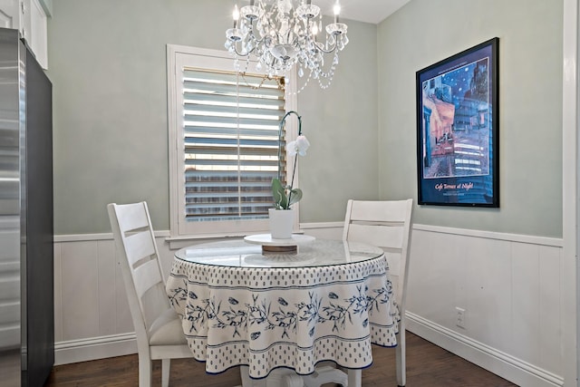 dining space with a wainscoted wall, dark wood finished floors, and a notable chandelier