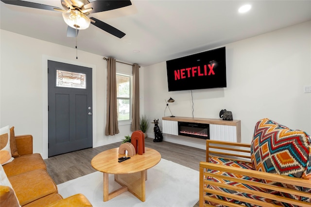 living area featuring light wood-type flooring, a ceiling fan, and a glass covered fireplace