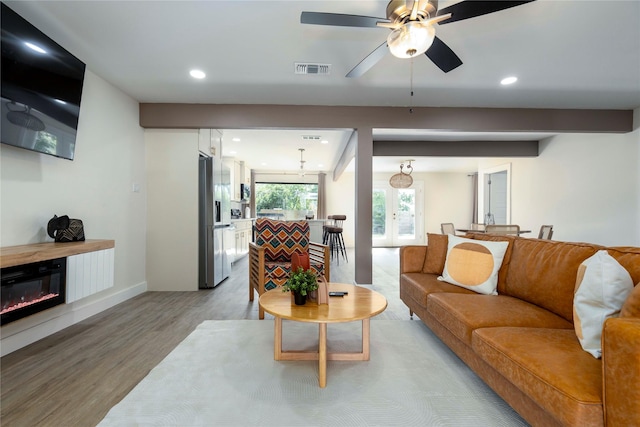 living room featuring recessed lighting, visible vents, light wood-type flooring, beam ceiling, and a glass covered fireplace