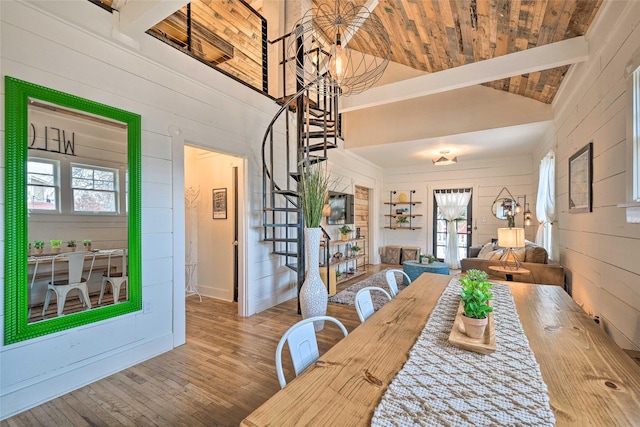 dining room with lofted ceiling with beams, wood ceiling, wooden walls, wood finished floors, and stairs