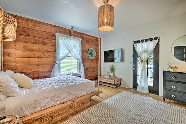 bedroom featuring access to outside, light wood-type flooring, visible vents, and wooden walls