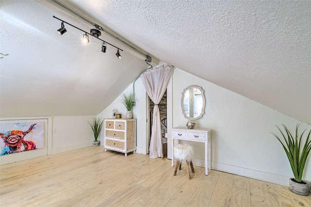 bonus room featuring a textured ceiling, vaulted ceiling, light wood-type flooring, and baseboards