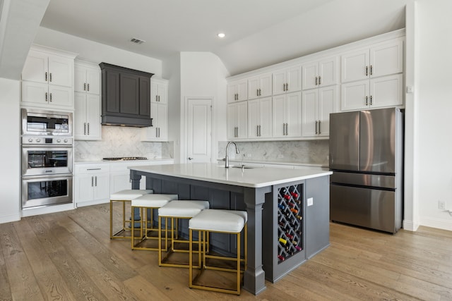 kitchen featuring stainless steel appliances, an island with sink, light countertops, and white cabinets