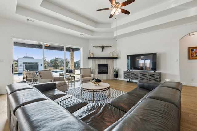 living room featuring arched walkways, a fireplace, a raised ceiling, wood finished floors, and baseboards