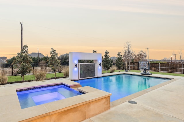 pool at dusk featuring a pool with connected hot tub, fence, and a patio