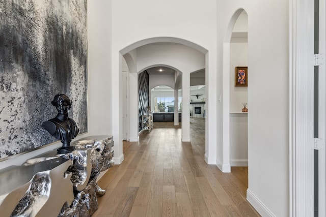 corridor featuring light wood-style floors, baseboards, and arched walkways