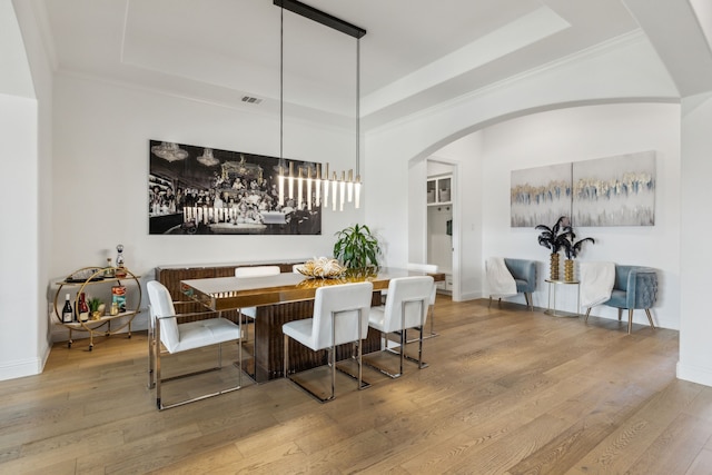 dining space featuring arched walkways, a tray ceiling, wood finished floors, and baseboards