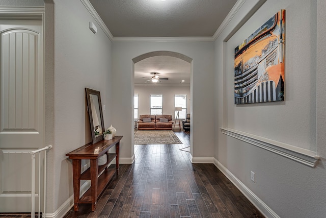 hallway with arched walkways, dark wood-style flooring, baseboards, and crown molding