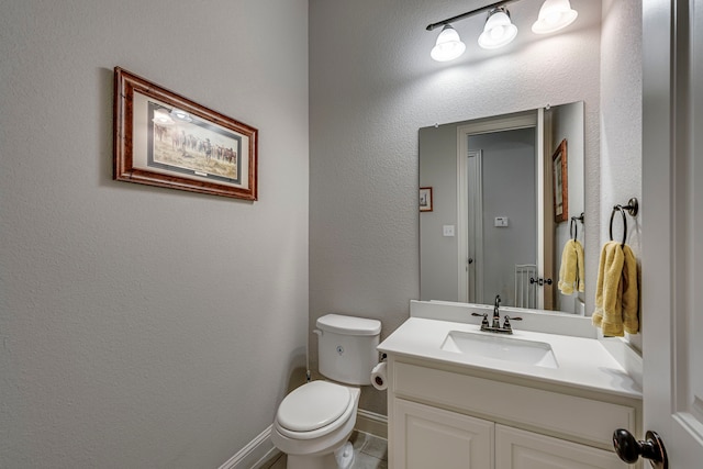 bathroom featuring toilet, a textured wall, baseboards, and vanity