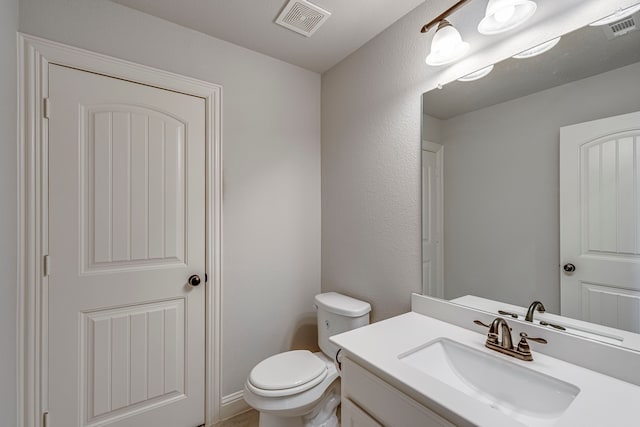 half bath featuring visible vents, a textured wall, vanity, and toilet